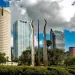 Tampa's skyline features tall skyscrapers and modern sculptures under a bright sky.